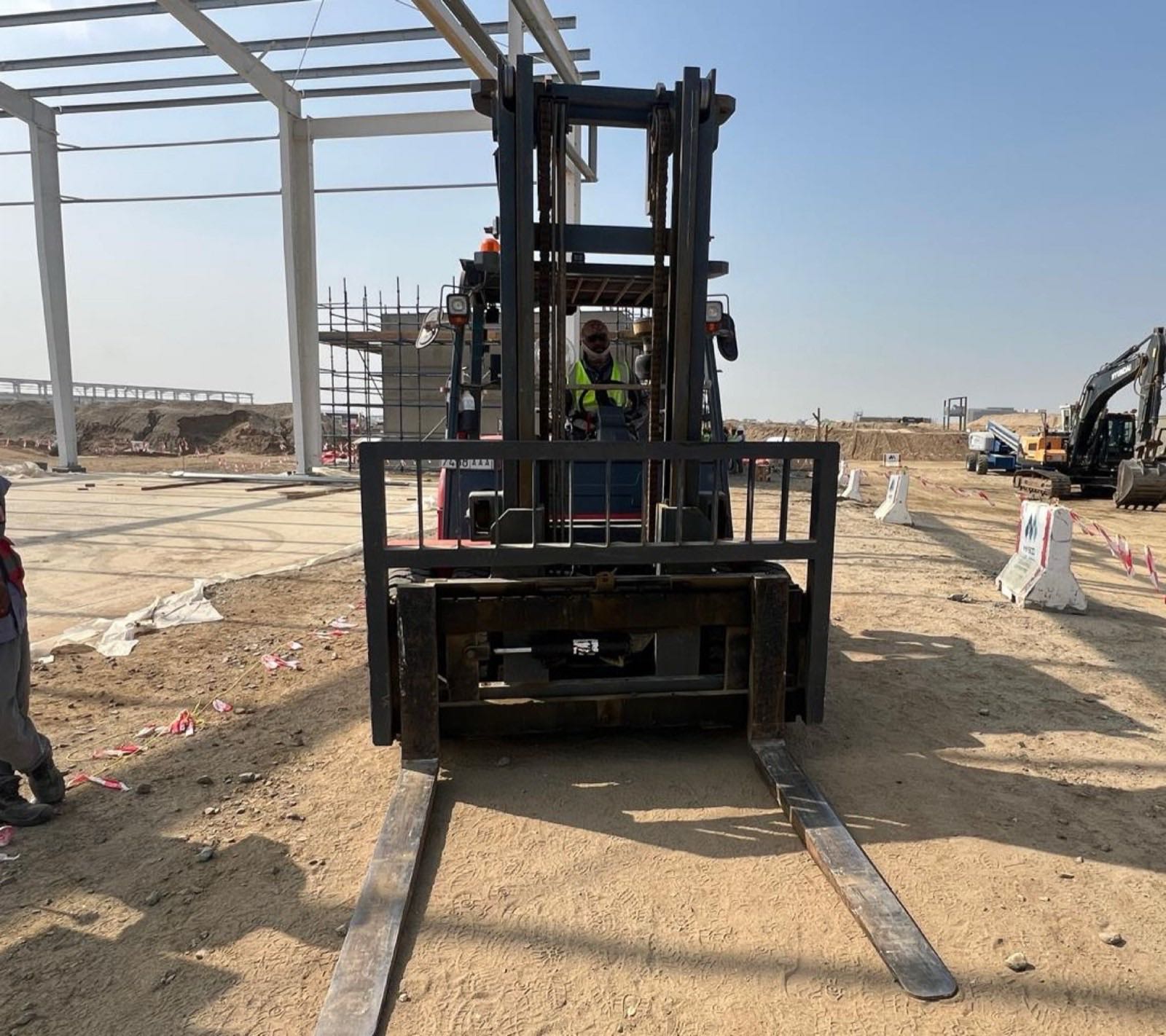 A forklift working an open storage yard beside a steel-frame structure
